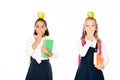 two shocked multicultural schoolgirls with apples on heads covering mouths with hands isolated on white. Royalty Free Stock Photo