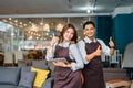 two shop assistants in aprons show thumbs up to the camera