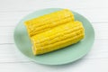 Two short boiled corn cobs on a green plate