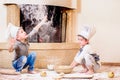 Two siblings - boy and girl - in chef`s hats near the fireplace sitting on the kitchen floor soiled with flour, playing with food Royalty Free Stock Photo