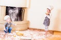 Two siblings - boy and girl - in chef`s hats near the fireplace sitting on the kitchen floor soiled with flour, playing with food Royalty Free Stock Photo