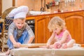 Two siblings - boy and girl - in chef`s hats sitting on the kitchen floor soiled with flour, playing with food, making mess and ha Royalty Free Stock Photo