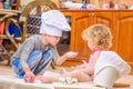 Two siblings - boy and girl - in chef`s hats sitting on the kitchen floor soiled with flour, playing with food, making mess and ha Royalty Free Stock Photo