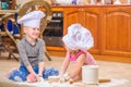 Two siblings - boy and girl - in chef`s hats sitting on the kitchen floor soiled with flour, playing with food, making mess and ha Royalty Free Stock Photo