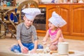 Two siblings - boy and girl - in chef`s hats sitting on the kitchen floor soiled with flour, playing with food, making mess and ha Royalty Free Stock Photo