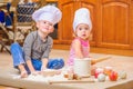 Two siblings - boy and girl - in chef`s hats sitting on the kitchen floor soiled with flour, playing with food, making mess and ha Royalty Free Stock Photo