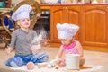 Two siblings - boy and girl - in chef`s hats sitting on the kitchen floor soiled with flour, playing with food, making mess and ha