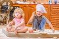 Two siblings - boy and girl - in chef`s hats sitting on the kitchen floor soiled with flour, playing with food, making mess and ha Royalty Free Stock Photo