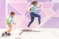 Two siblings, a boy and a girl, jumping and running in front of a pink and purple colored wall on the way to school. Back to schoo Royalty Free Stock Photo