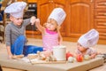 Boy and girl and a newborn kid with them in chef`s hats sitting on the kitchen floor soiled with flour