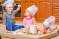 Boy and girl and a newborn kid with them in chef`s hats sitting on the kitchen floor soiled with flour