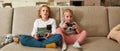 Two siblings, little boy and girl looking focused, playing video games using joystick or controller while sitting Royalty Free Stock Photo