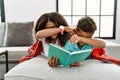Two siblings lying on the sofa reading a book smiling cheerful playing peek a boo with hands showing face