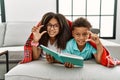 Two siblings lying on the sofa reading a book smiling and confident gesturing with hand doing small size sign with fingers looking Royalty Free Stock Photo