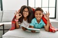 Two siblings lying on the sofa reading a book smiling positive doing ok sign with hand and fingers Royalty Free Stock Photo