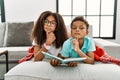 Two siblings lying on the sofa reading a book thinking concentrated about doubt with finger on chin and looking up wondering