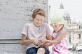 Two siblings sharing drinking water plastic bottle in city travel during hot summer day