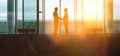 Two silhouette businessmen shaking hands in the airport lobby