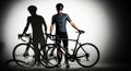 Two silhouetted cyclists stand with their bikes in dramatic studio lighting casting long shadows across the floor Royalty Free Stock Photo