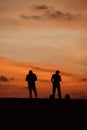 Two silhouetted figures standing against orange sunset skies Royalty Free Stock Photo