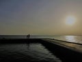 Two silhouettes accompany the sun on the pier