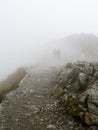 Two silhouettes of people in thick fog on rocky hiking trail in the mountains