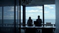 Two silhouettes shaking hands in modern hall. Business partners leaving office Royalty Free Stock Photo