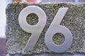 Two silver metallic digits showing the number ninety six fixed on a grey wall