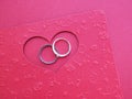 Two silver rings on a red heart-shaped card over red paper background with copy space. Royalty Free Stock Photo