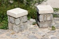 Two single seats stone and concrete public benches on stone tiles foundation with dense plants in background