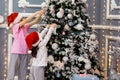 Two sister girls in red caps and pajamas decorate the Christmas tree with balls Royalty Free Stock Photo