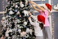 Two sister girls in red caps and pajamas decorate the Christmas tree with balls Royalty Free Stock Photo