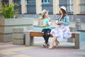 Two sisters, a beautiful brunette girl and a young girl walking in the city, sitting on a bench with coffee in hands and Royalty Free Stock Photo