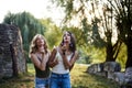 Two sisters, blowing soap bubbles in park, Young pretty girls, wearing jeans shorts, green khaki beige tops, having fun outside. Royalty Free Stock Photo