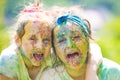 Two sisters child girls celebrate Indian holi festival with colorful paint powder on faces.