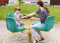 Two sisters are having fun on the carousel. Little girl has fun in the outdoor playground. The older sister rides the younger