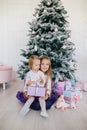 Two sisters at home with Christmas tree and presents. Happy children girls with Christmas gift boxes and decorations.