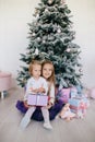 Two sisters at home with Christmas tree and presents. Happy children girls with Christmas gift boxes and decorations.