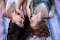 Two sisters, lying on blanket in park, looking at each other, making amazed wondering face expressions. Young pretty girls,