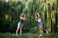 Two sisters, making blowing soap bubbles in park in summer. Young pretty girls, wearing jeans shorts and green beige tops, having Royalty Free Stock Photo