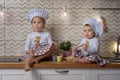 Two sisters in cook hats sit on the kitchen table and drink tea with cookies