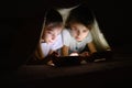 Two sisters play games on their smartphones at night under the covers.