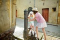 Two sisters playing with drinking water fountain in Montalcino town, located on top of a hill top and surrounded by vineyards,