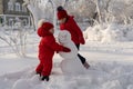 Two sisters in red jackets and hats are making a snowman in a winter park. In winter, children play alone outside. Royalty Free Stock Photo