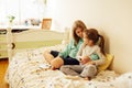 Two sisters are sitting on the bed and listening to cd player. Girls share one headphones for two. Older girl takes care of