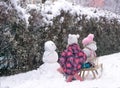 Two sisters on sled looking to snowman at snow day in park. Royalty Free Stock Photo