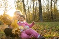 Two sisters spending time in autumn park and showing collected orange leaves