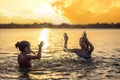 Two sisters splashing water playing in the lake at sunset background