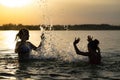 Two sisters splashing water playing in the lake at sunset background