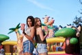 Two sisters, standing is front of attraction in theme park, holding popcorn in paper box, smiling, having fun. Pretty girls.